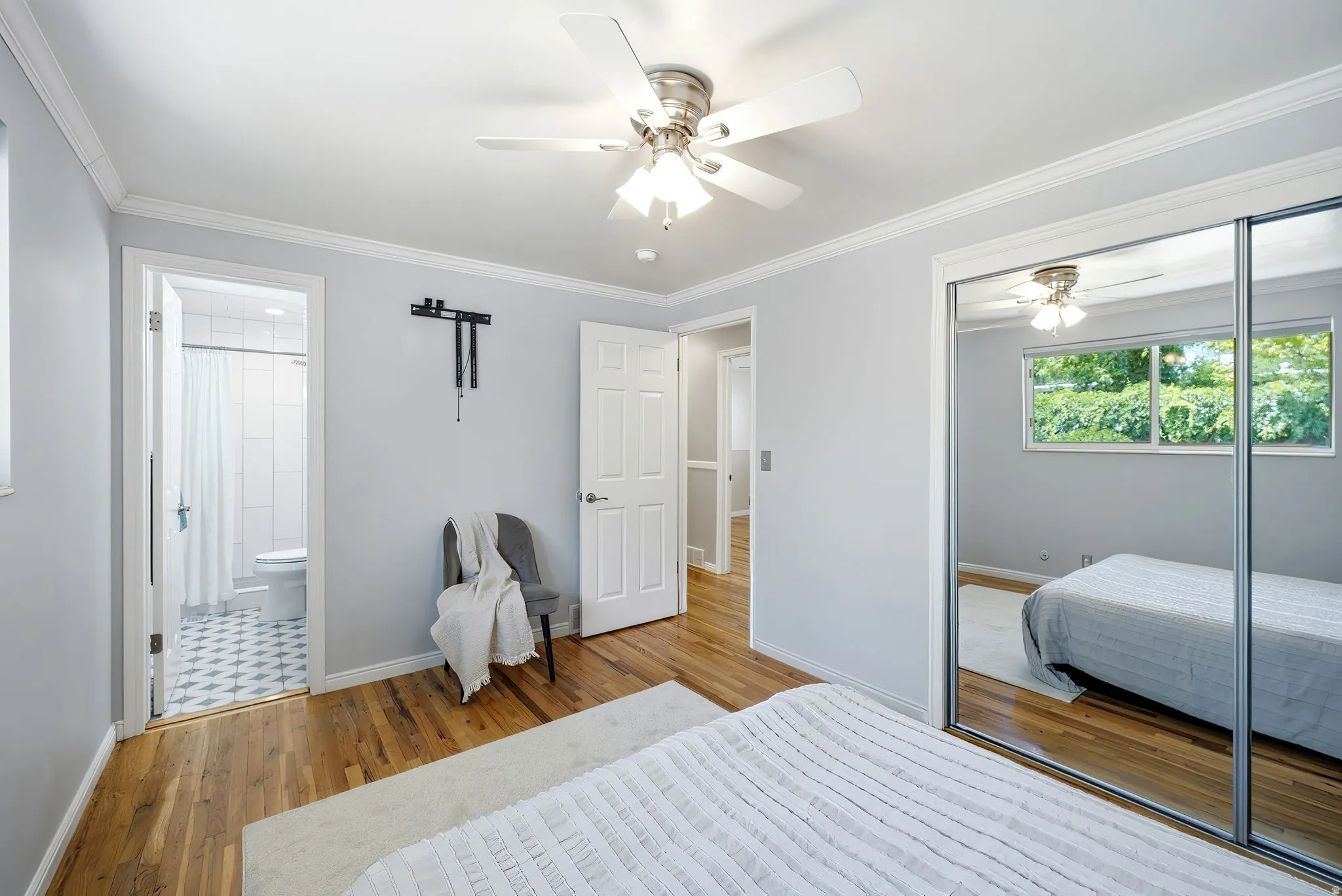 Master Bedroom featuring wood-finish flooring, white ceiling fan with integrated lighting, mirrored sliding closet doors, and crown molding