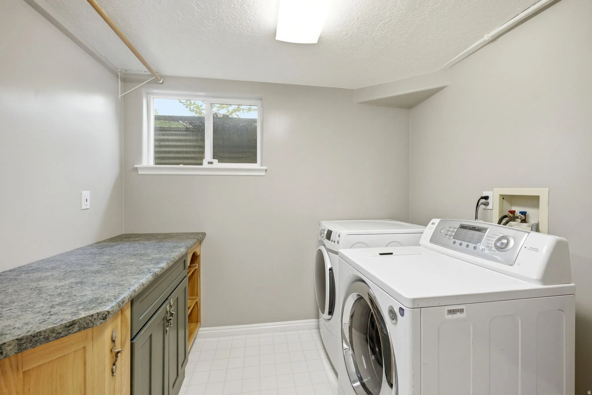 Dedicated utility room featuring a built-in counter with cabinet storage, a window, and white tile flooring