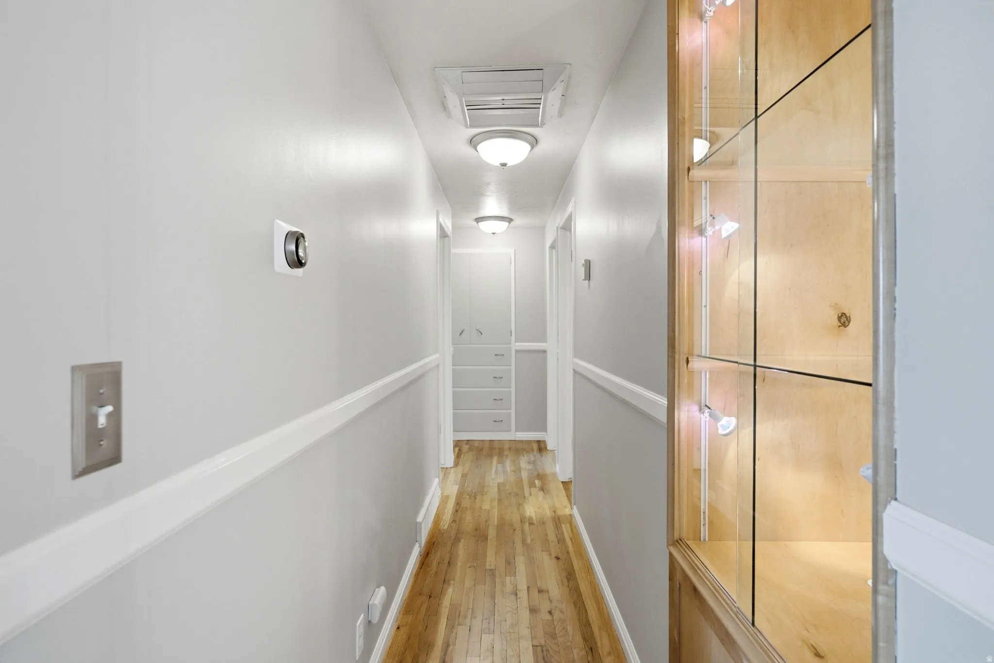Hallway featuring wood-finish flooring, light gray walls with chair rail molding, and multiple flush-mount light fixtures