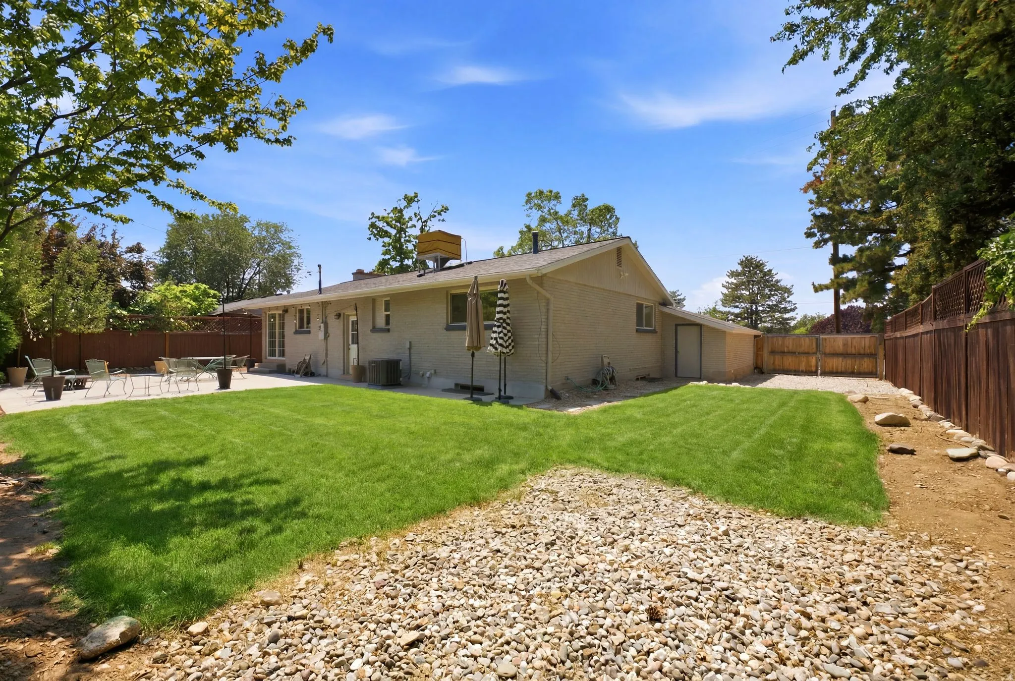 Expansive backyard with a large concrete patio, manicured lawn, and mature perimeter trees
