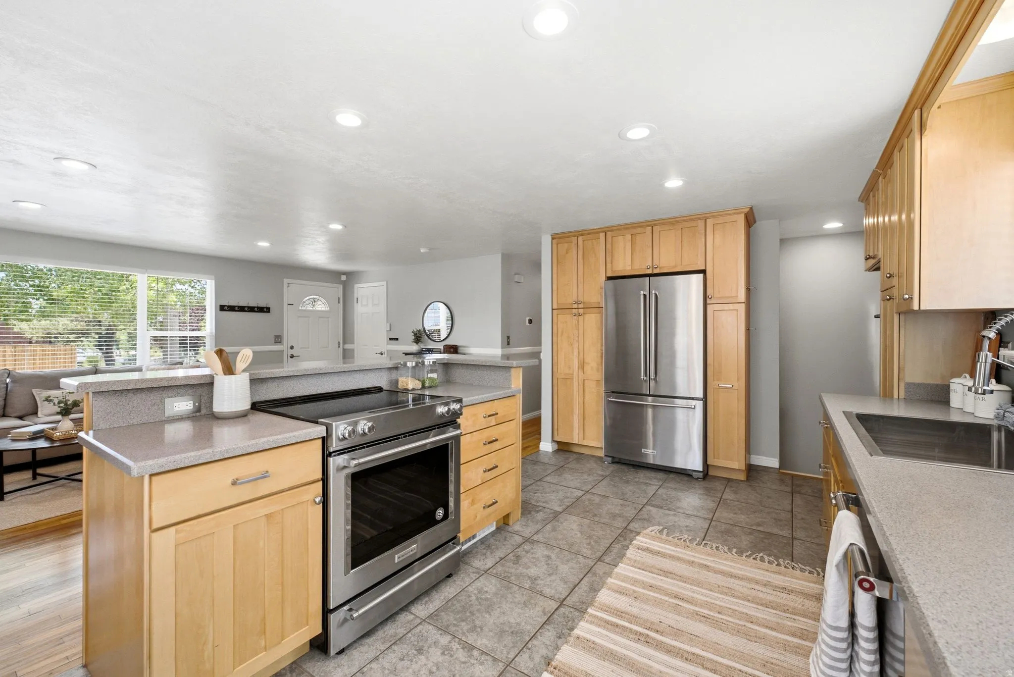Kitchen featuring wood cabinetry, stainless steel appliances, grey stone-finish countertops, tile flooring, and recessed lighting