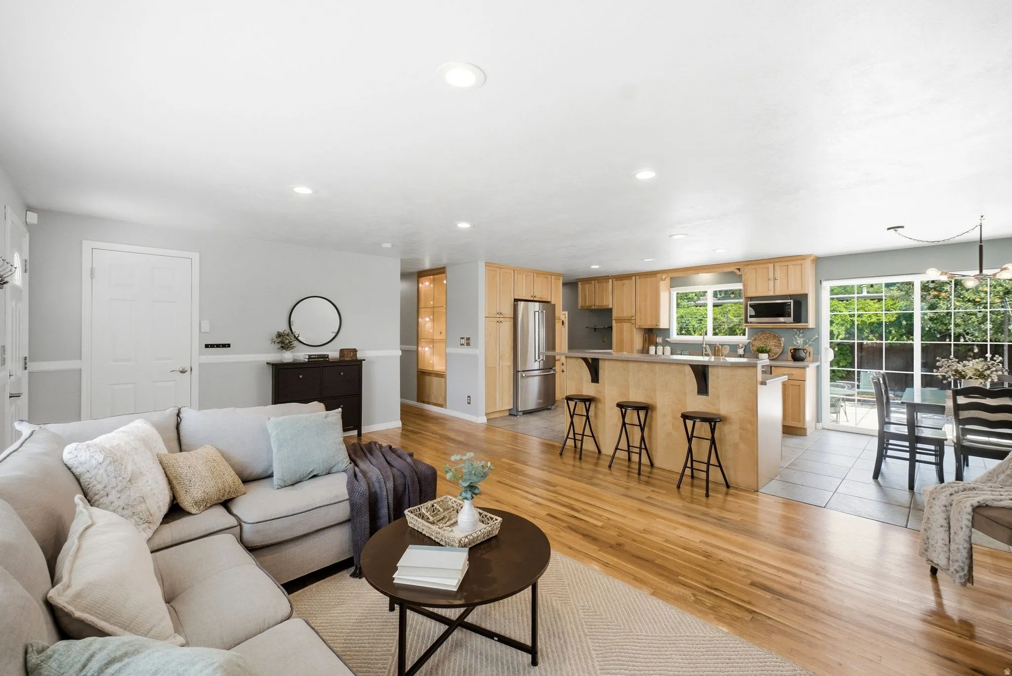 Open-concept living space featuring wood-finish flooring, recessed lighting, a kitchen island with seating, a built-in microwave, and a glass sliding door
