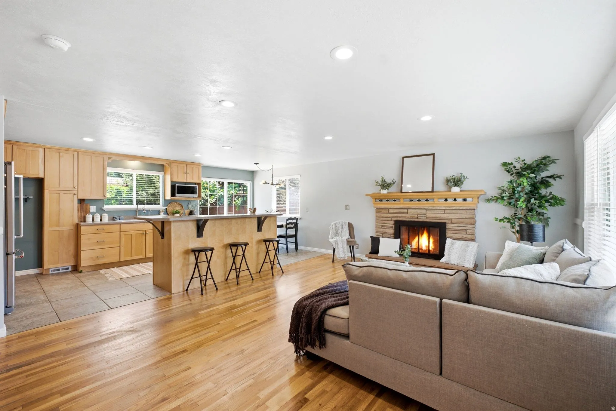 Open-concept living area featuring wood-finish flooring, a stone-surround fireplace with a wood mantle, and recessed lighting