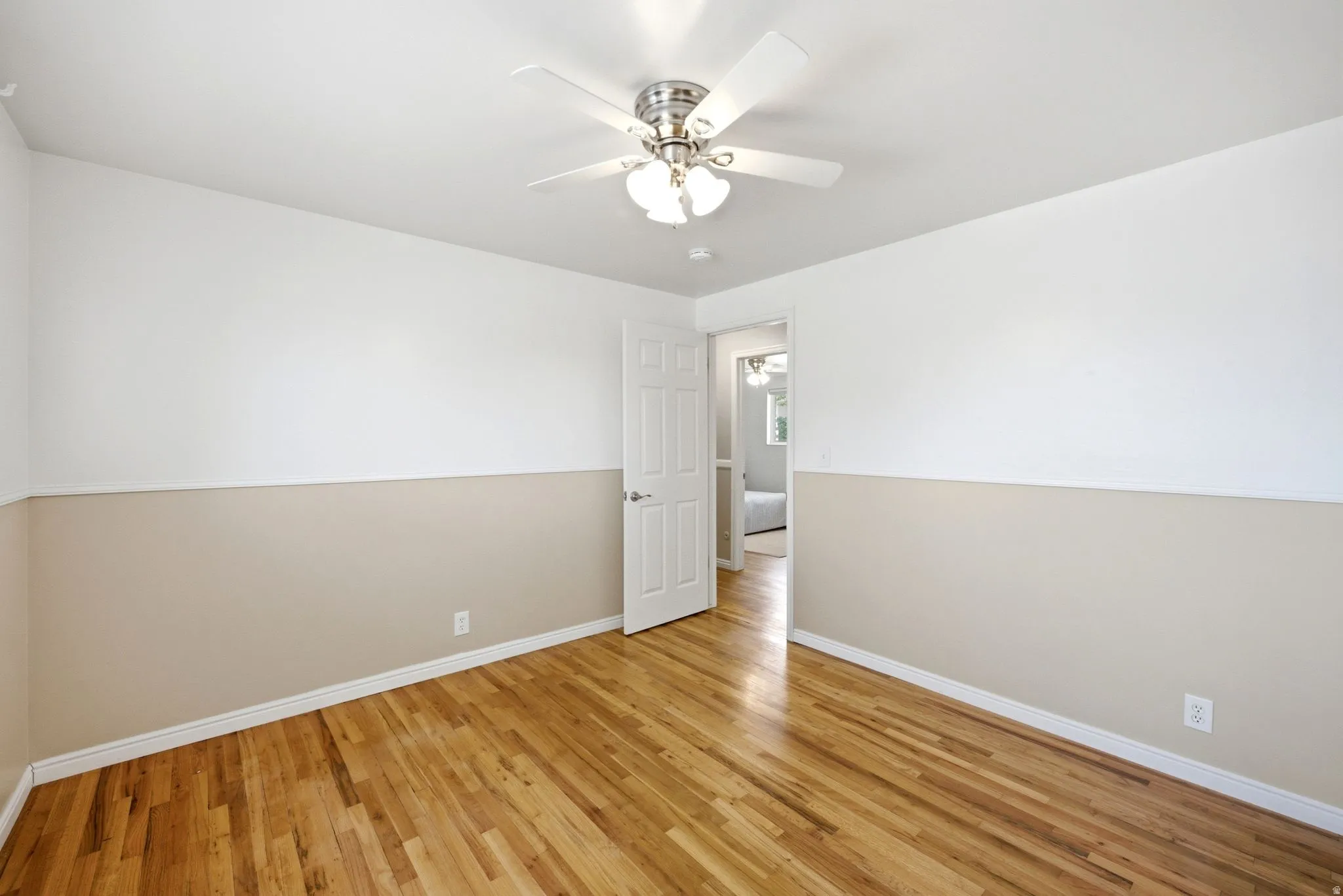 Room featuring wood-finish flooring, a neutral two-tone wall treatment, white trim, and a ceiling fan with integrated lighting