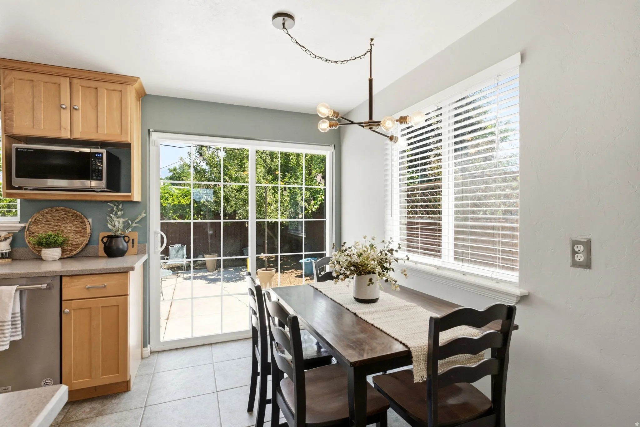 Dining area with tiled flooring, a modern chandelier, and a large window featuring blinds