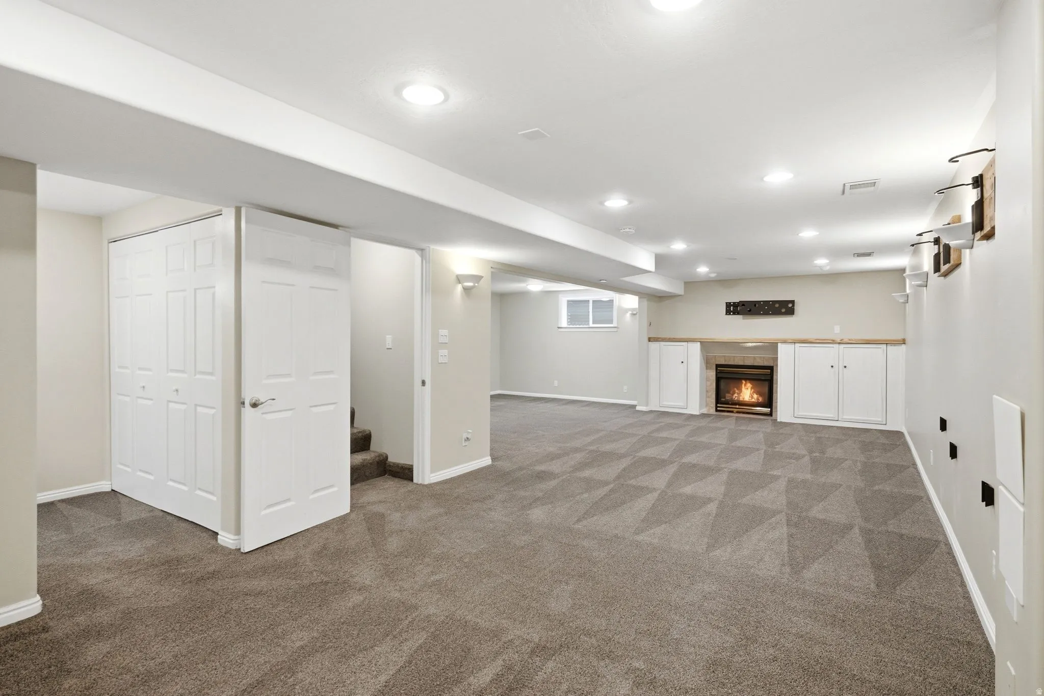 Spacious finished basement featuring patterned carpet, recessed lighting, built-in fireplace with surround cabinetry, and a window