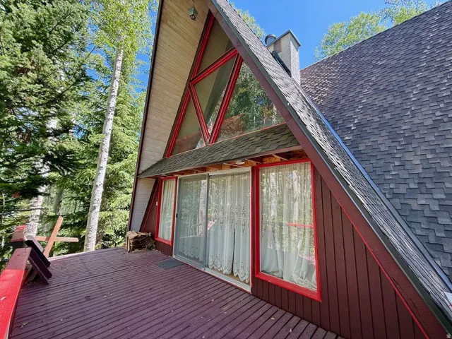 A-frame exterior featuring a prominent red-framed window wall, expansive wood deck, and a shingle roof