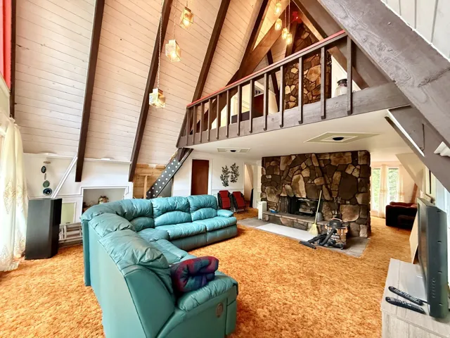 Vaulted wood-paneled ceilings with exposed beams, stone fireplace, and a loft space with wood railing