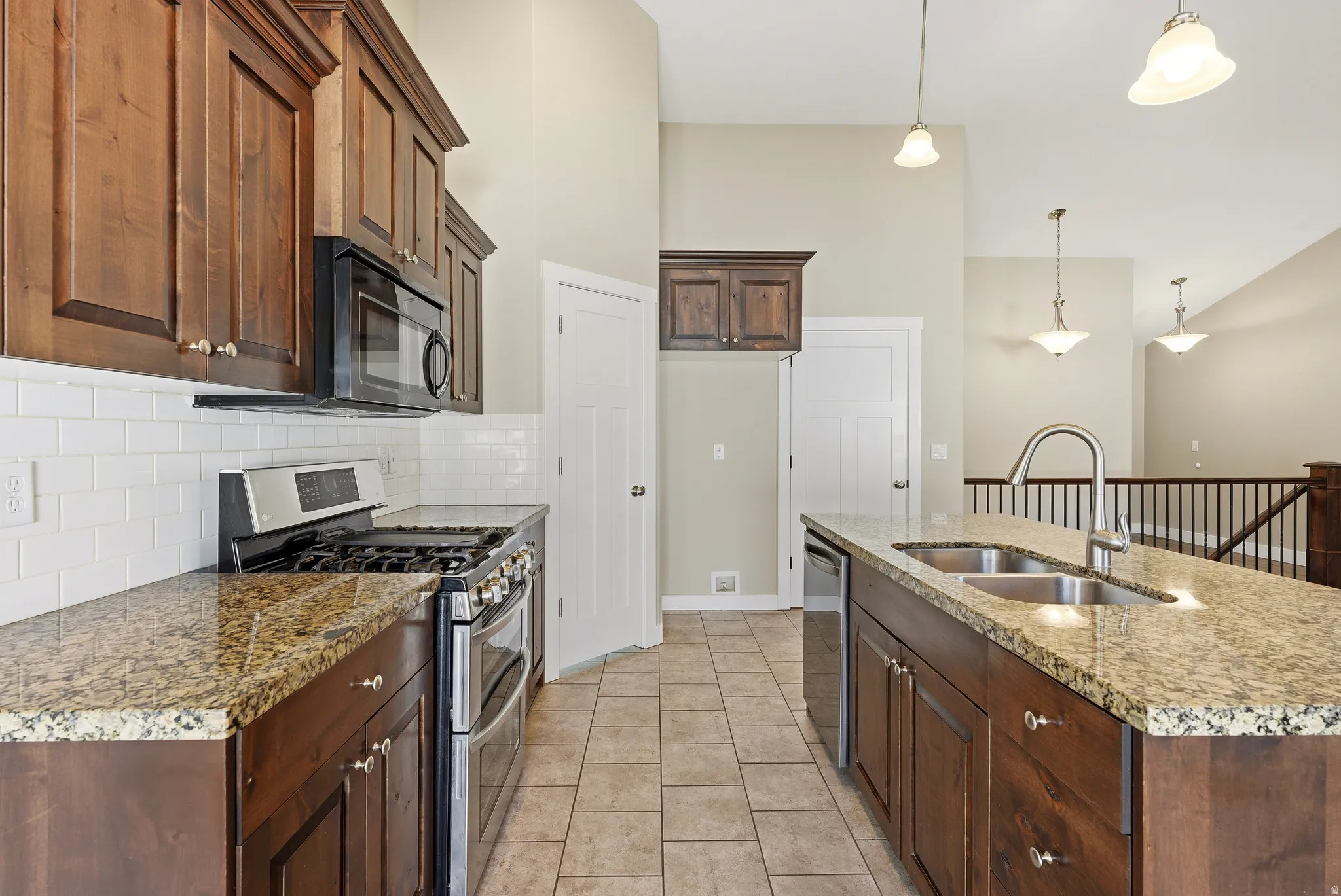 Kitchen featuring wood cabinetry,  a large pantry, stainless steel appliances, a gas range, tile backsplash, granite countertops, and a kitchen island with a dual-basin sink