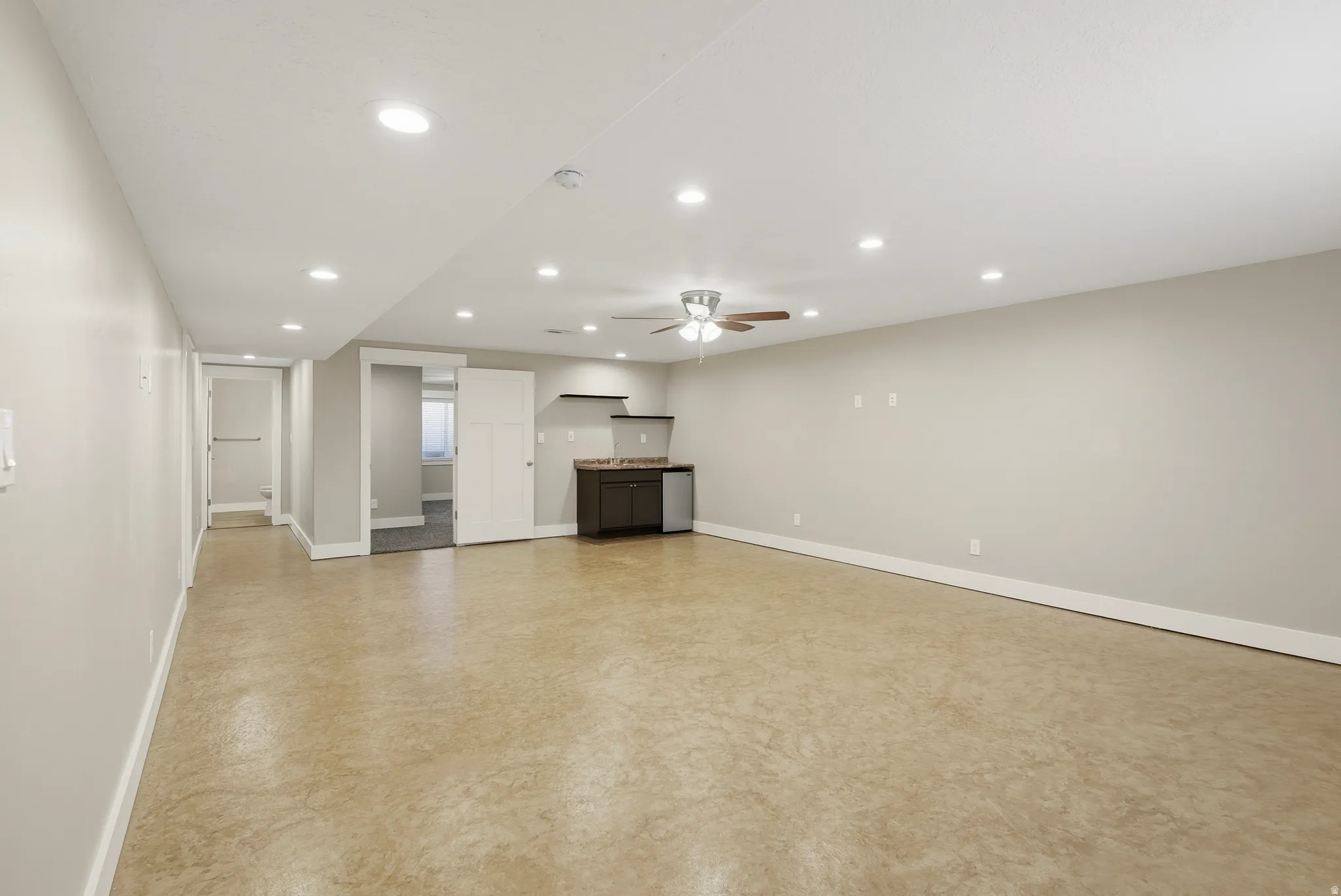 Spacious open-concept family room featuring light-toned flooring, recessed lighting, a wet bar with a space for a full-size fridge and more!
