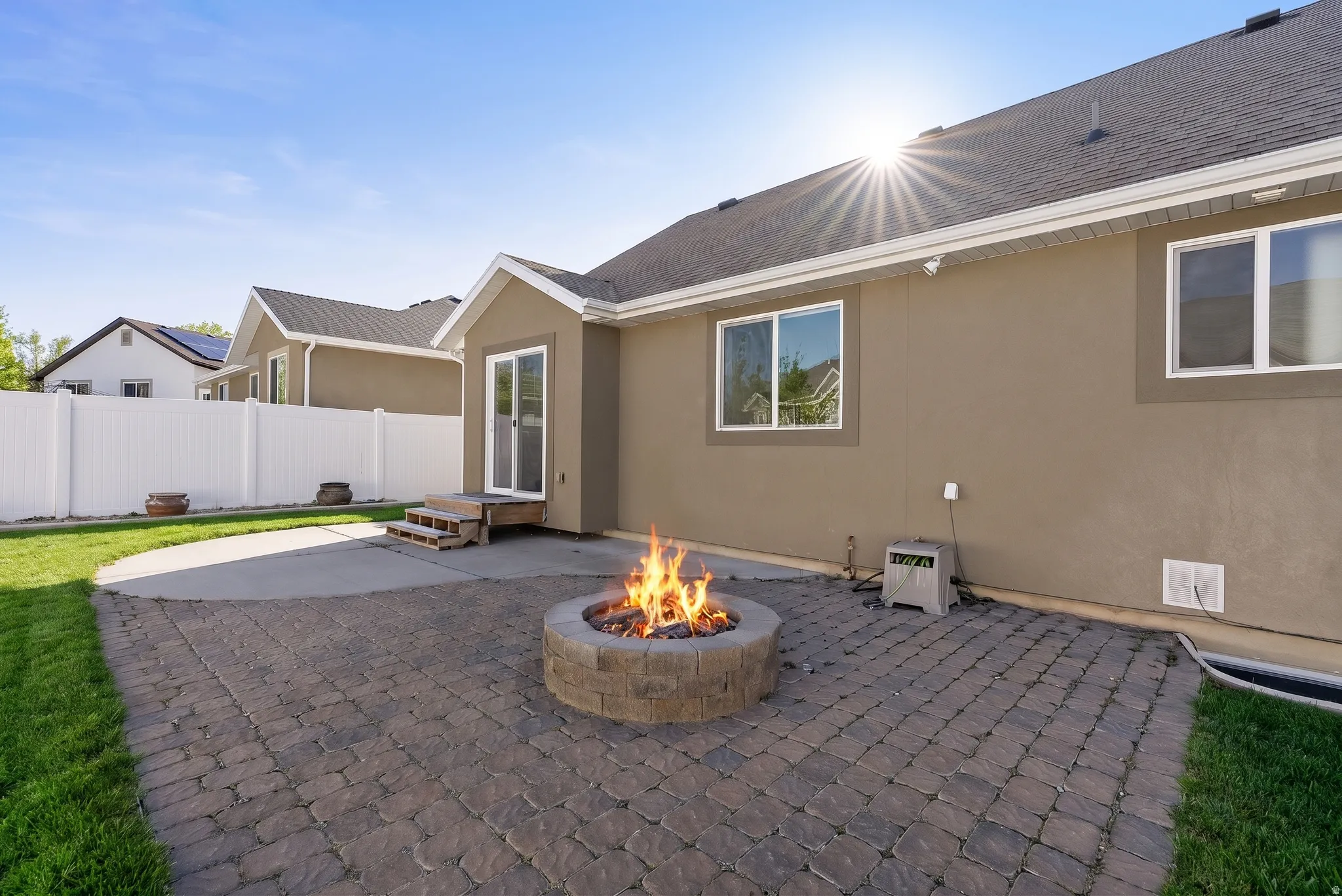 Backyard featuring a stone gas fire pit, paver patio, and a white vinyl privacy fence