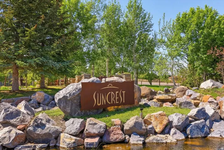 Community entrance featuring a metal sign, decorative boulders, a water feature, and mature trees