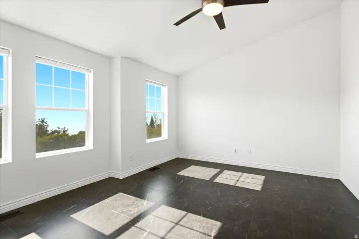 Spacious room featuring multiple double-hung windows, dark-toned tile flooring, a vaulted ceiling, and a ceiling fan with integrated lighting