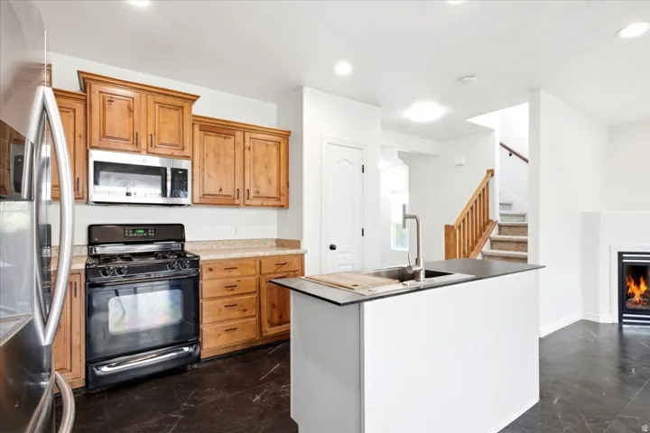 Open-concept kitchen featuring wood cabinetry, stainless steel microwave, black range, and a kitchen island with an undermount sink