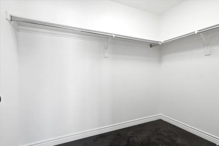 Corner closet featuring white walls, white trim, and a dark-finish floor