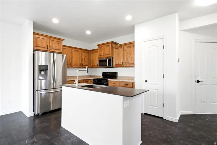 Kitchen featuring wood cabinetry, stainless steel appliances, an island with an undermount sink, and dark flooring
