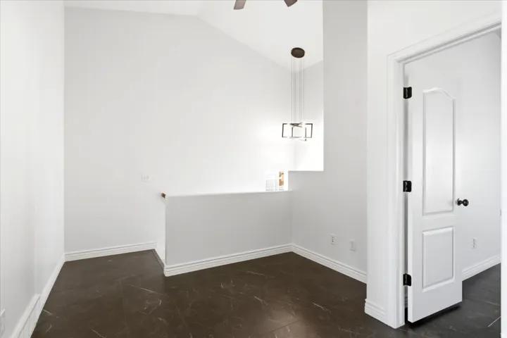 Vaulted ceiling with an overhead fan, dark stone-finish flooring, and white baseboards