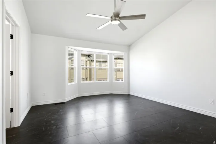 Bay window with multiple panes, dark tile flooring, white baseboards, and a ceiling fan with integrated lighting