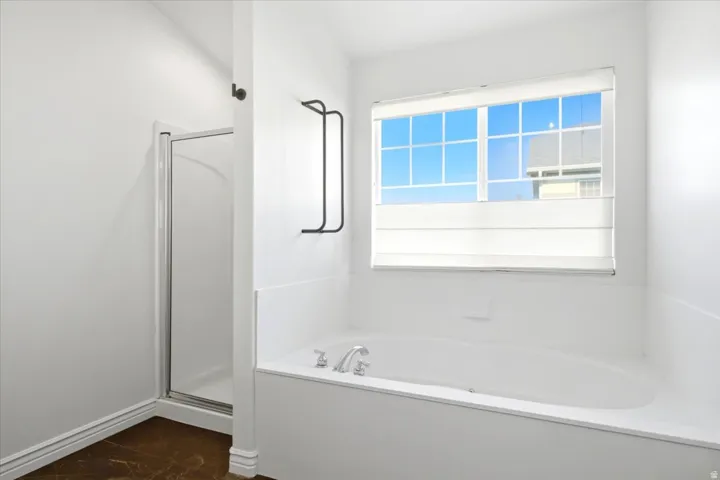 Spacious bathroom featuring a built-in bathtub with chrome fixtures, a large window with privacy blinds, and a separate glass-enclosed shower