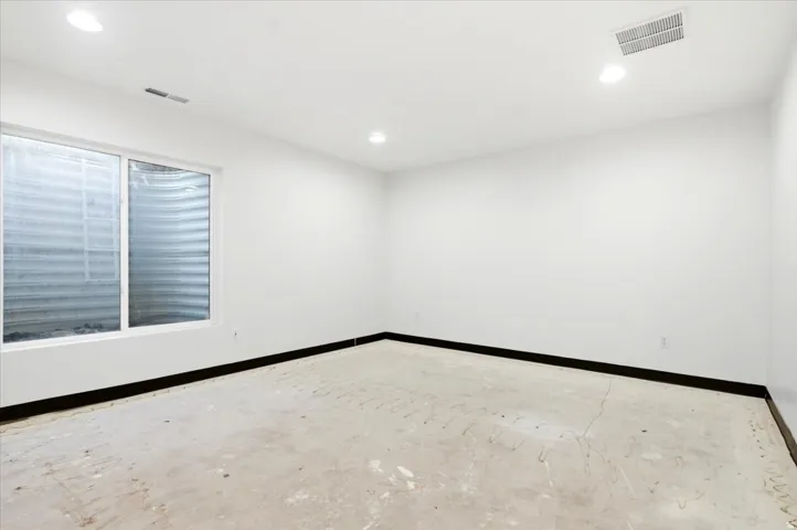 Spacious room featuring a large window, recessed lighting, white walls, and a black baseboard
