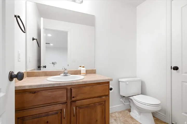 Bathroom featuring a wooden vanity with a laminate countertop and integrated sink, a white toilet, and textured tile flooring