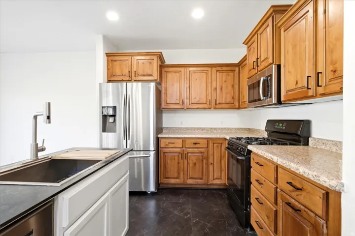 Kitchen featuring wood cabinetry with black hardware, stainless steel refrigerator, built-in microwave, and black gas range