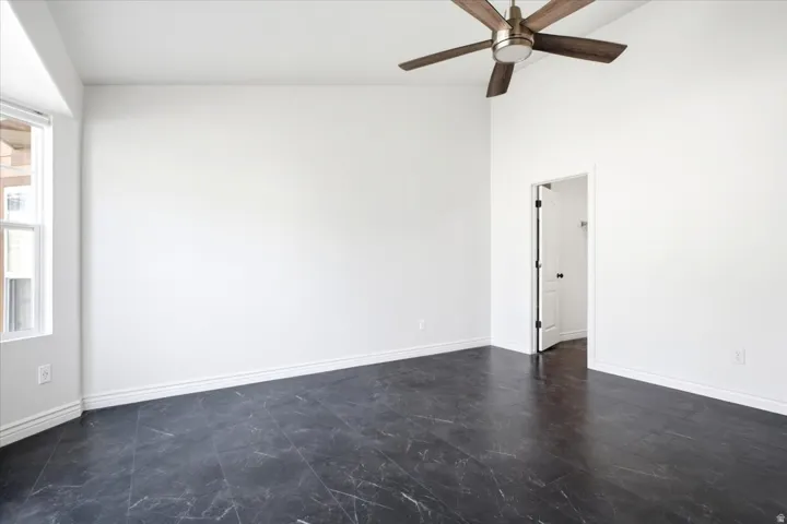 Spacious room with dark-toned flooring, white baseboards, and a contemporary ceiling fan with wood-finish blades