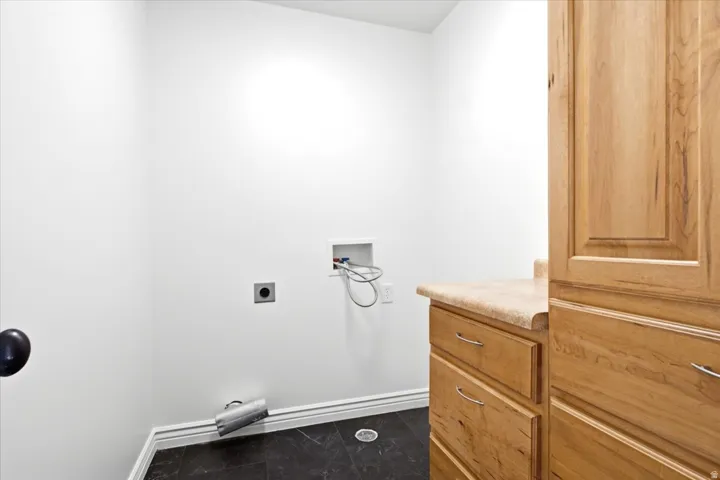 Utility room with dark tile flooring, white walls, and light wood cabinetry featuring a laminate countertop