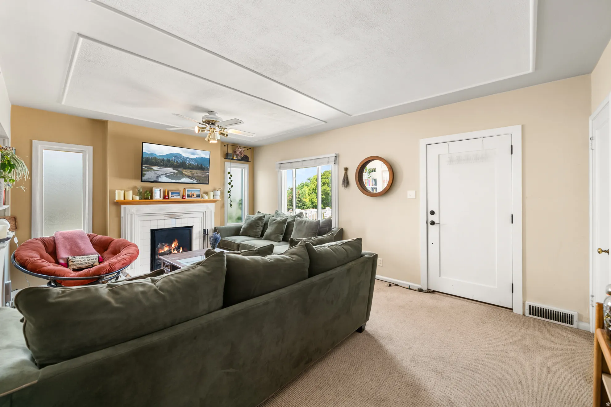Living room featuring a fireplace with a white mantel, ceiling fan, and recessed ceiling panels