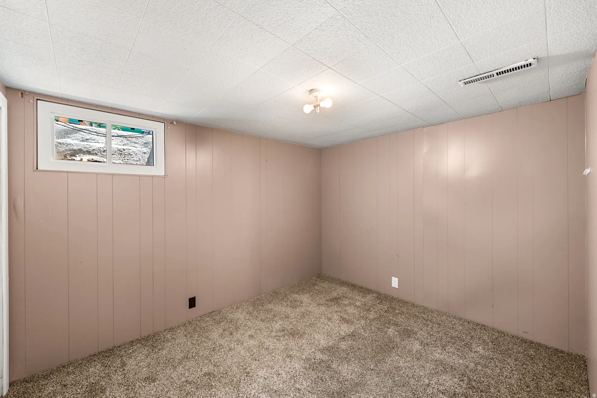 Room featuring neutral-toned paneled walls, a drop ceiling, recessed window, and textured carpeting