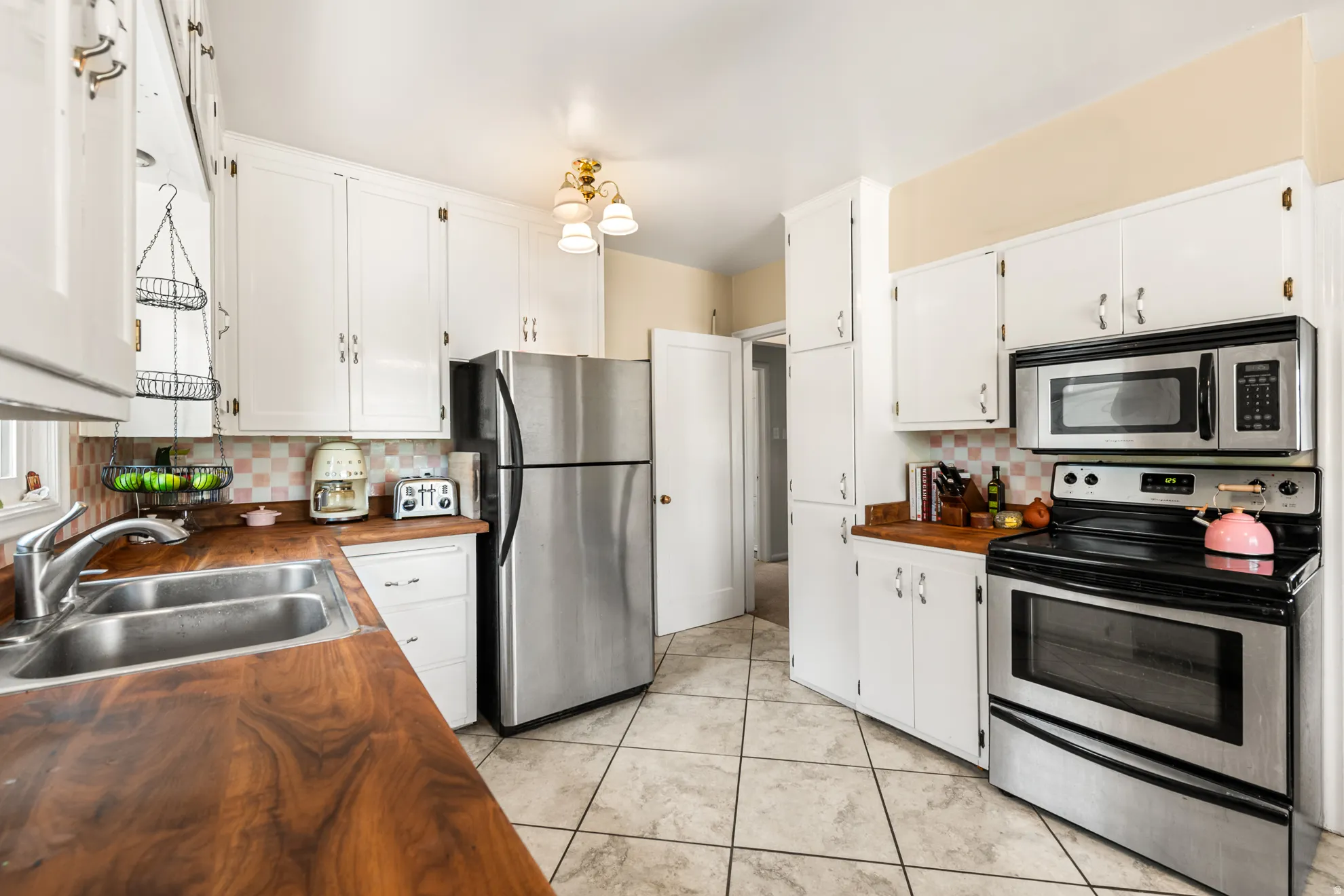 Kitchen featuring wood-finish countertops, white cabinetry, a double basin sink, and stainless steel appliances