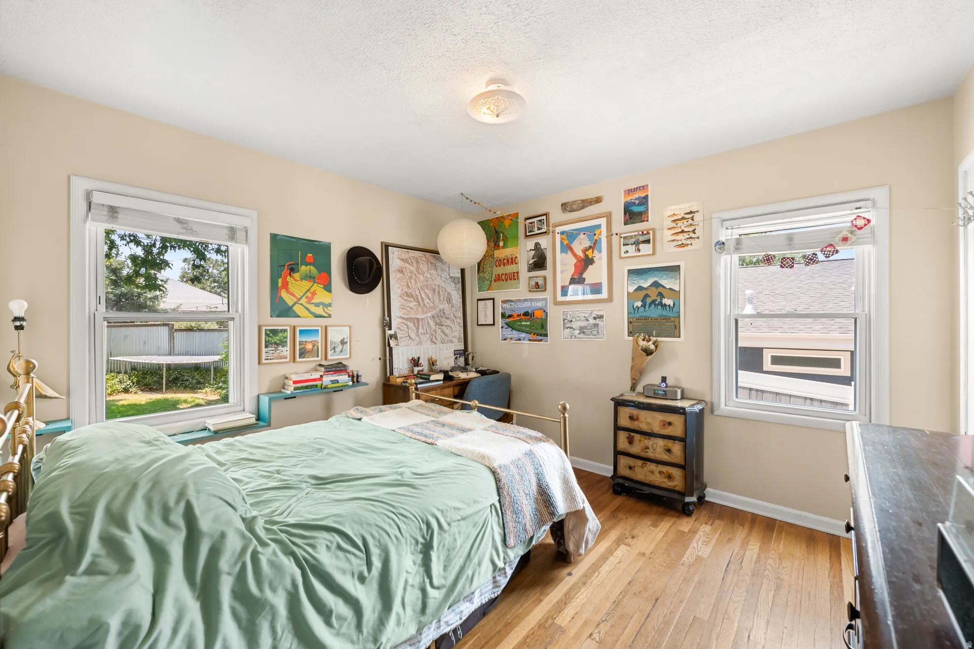 Bedroom featuring two windows, light-toned walls, and wood-finish flooring