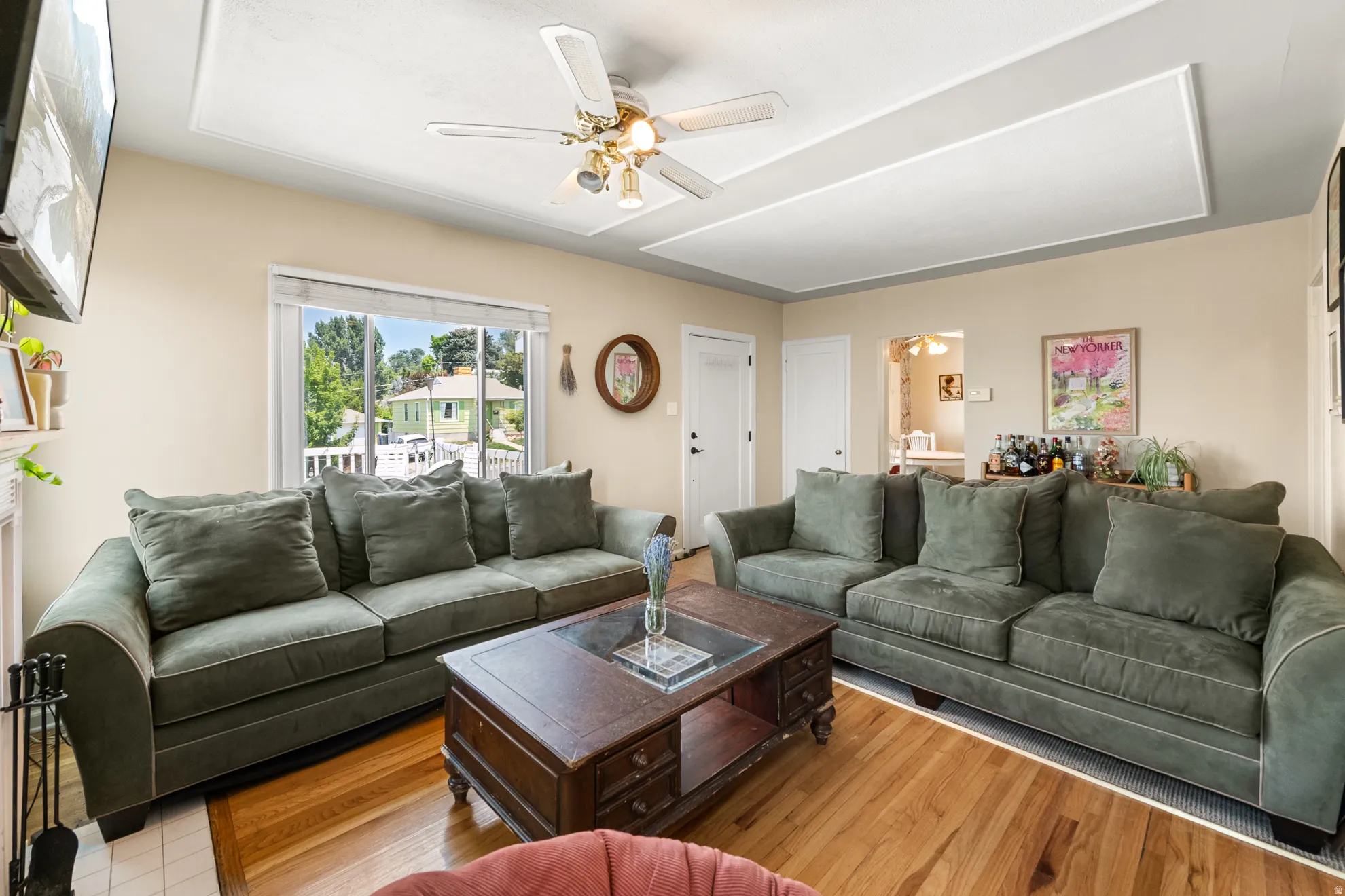 Living area featuring wood-finish flooring, a ceiling fan with integrated lighting, and a white framed window