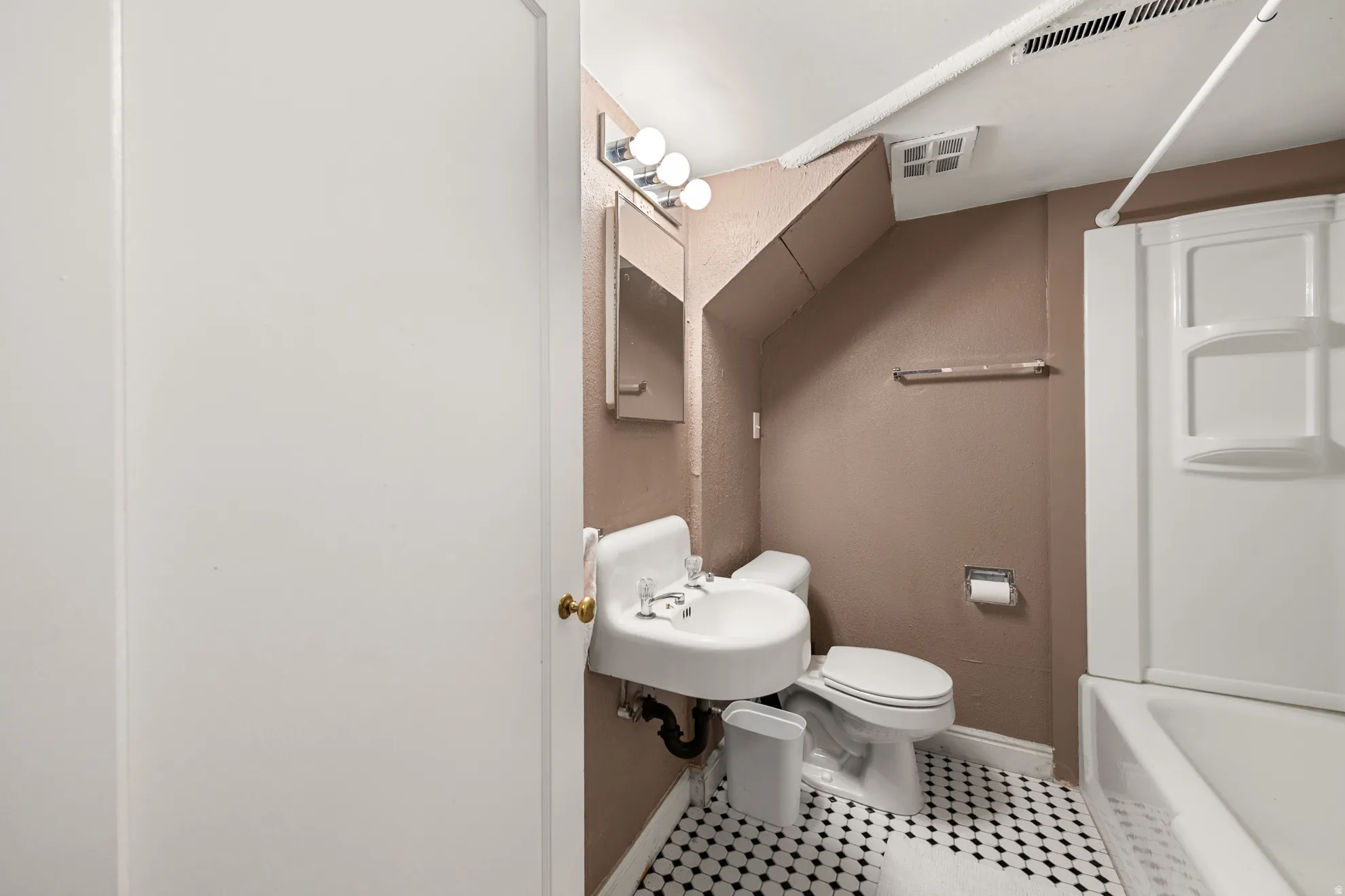 Compact bathroom featuring a wall-mounted sink, toilet, and combined shower/tub unit