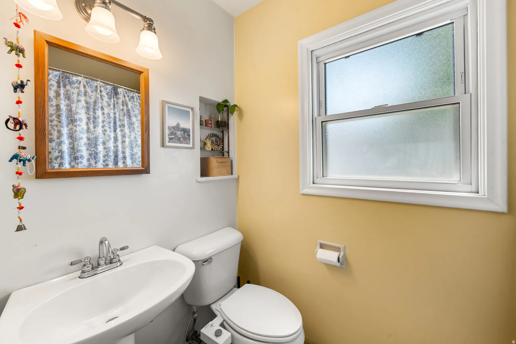 Bathroom featuring a pedestal sink with chrome faucet, a wall-mounted light fixture, and a built-in recessed shelf