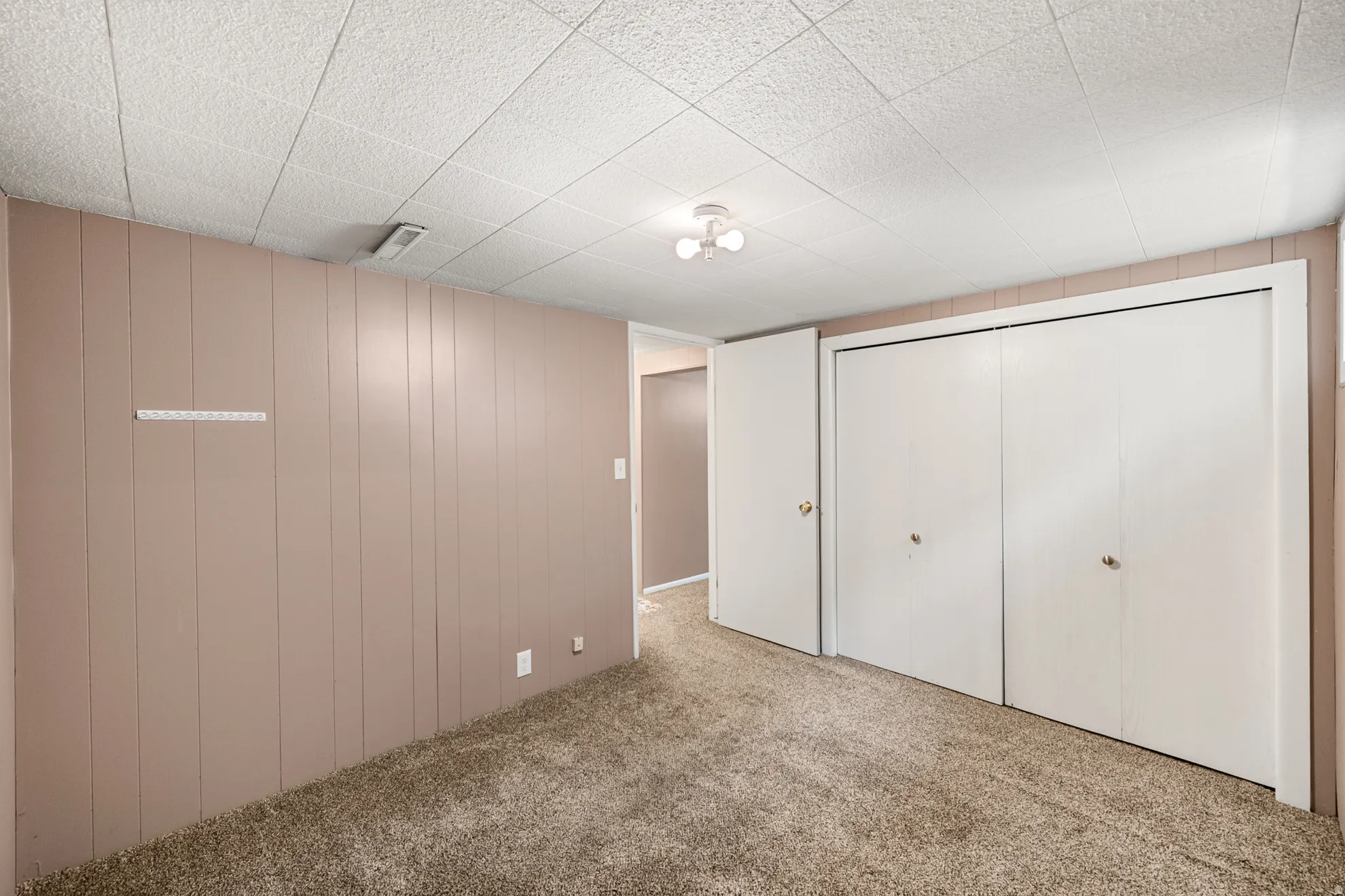 Carpeted room featuring vertical wood paneling and a drop ceiling