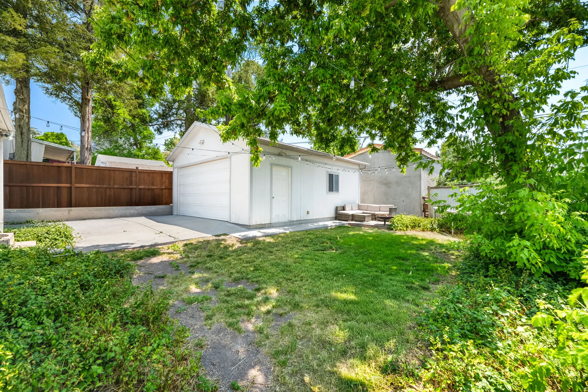 Detached garage with a roll-up door and side entry, featuring a paved driveway and concrete patio