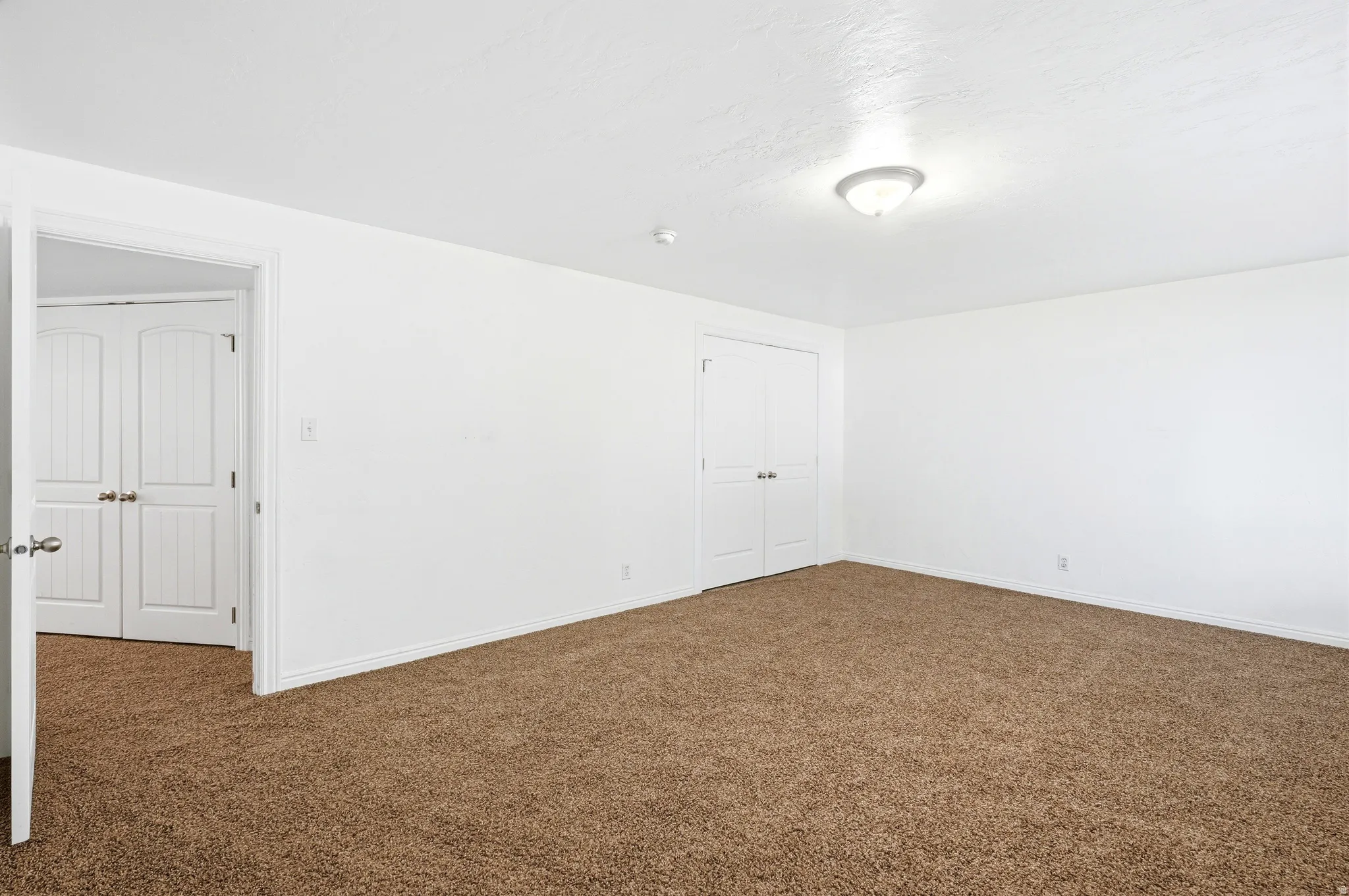 Bright room featuring neutral carpeting, white walls, a flush-mount ceiling light, and white paneled doors