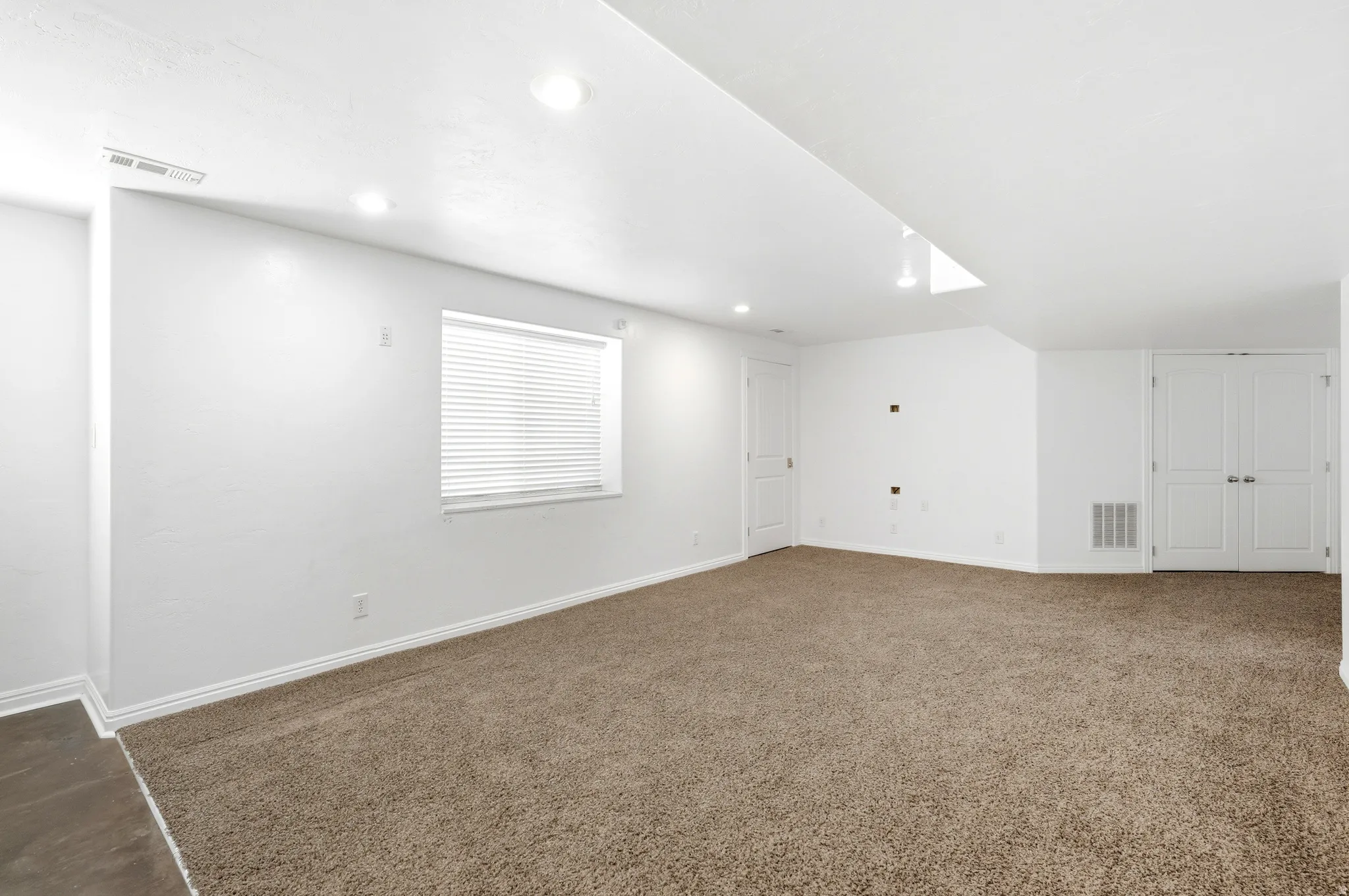 Open-concept room featuring neutral carpet flooring, recessed lighting, a white window blind, and two white double-panel doors