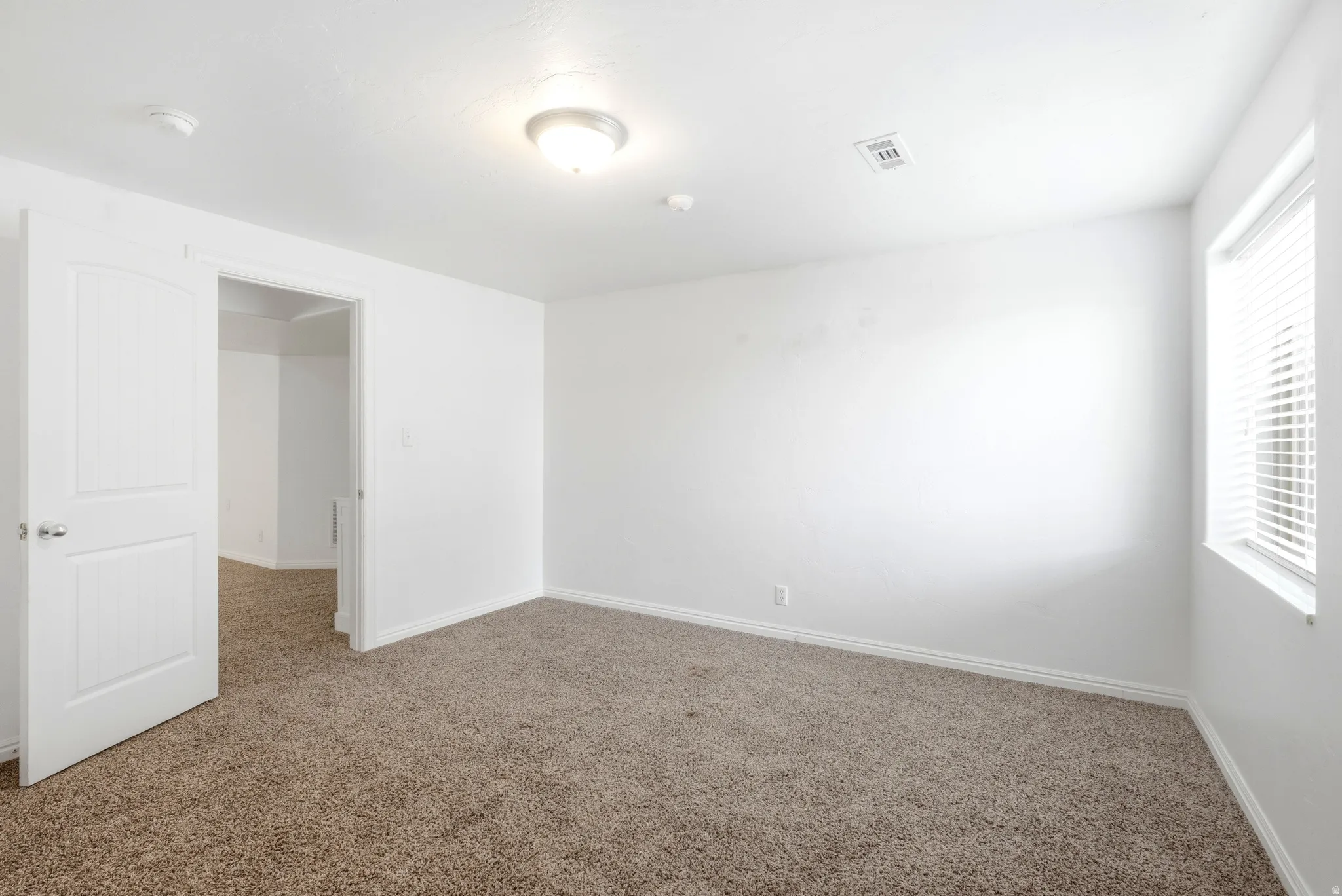 Carpeted room featuring white walls, a single window with blinds, and a paneled interior door