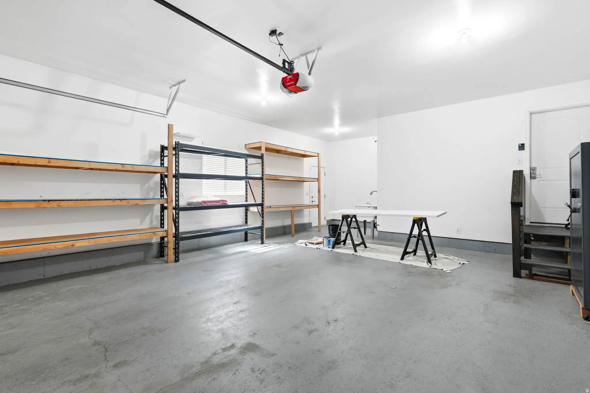 Spacious garage featuring a concrete floor, built-in shelving, overhead lighting, an overhead garage door opener, and a utility sink
