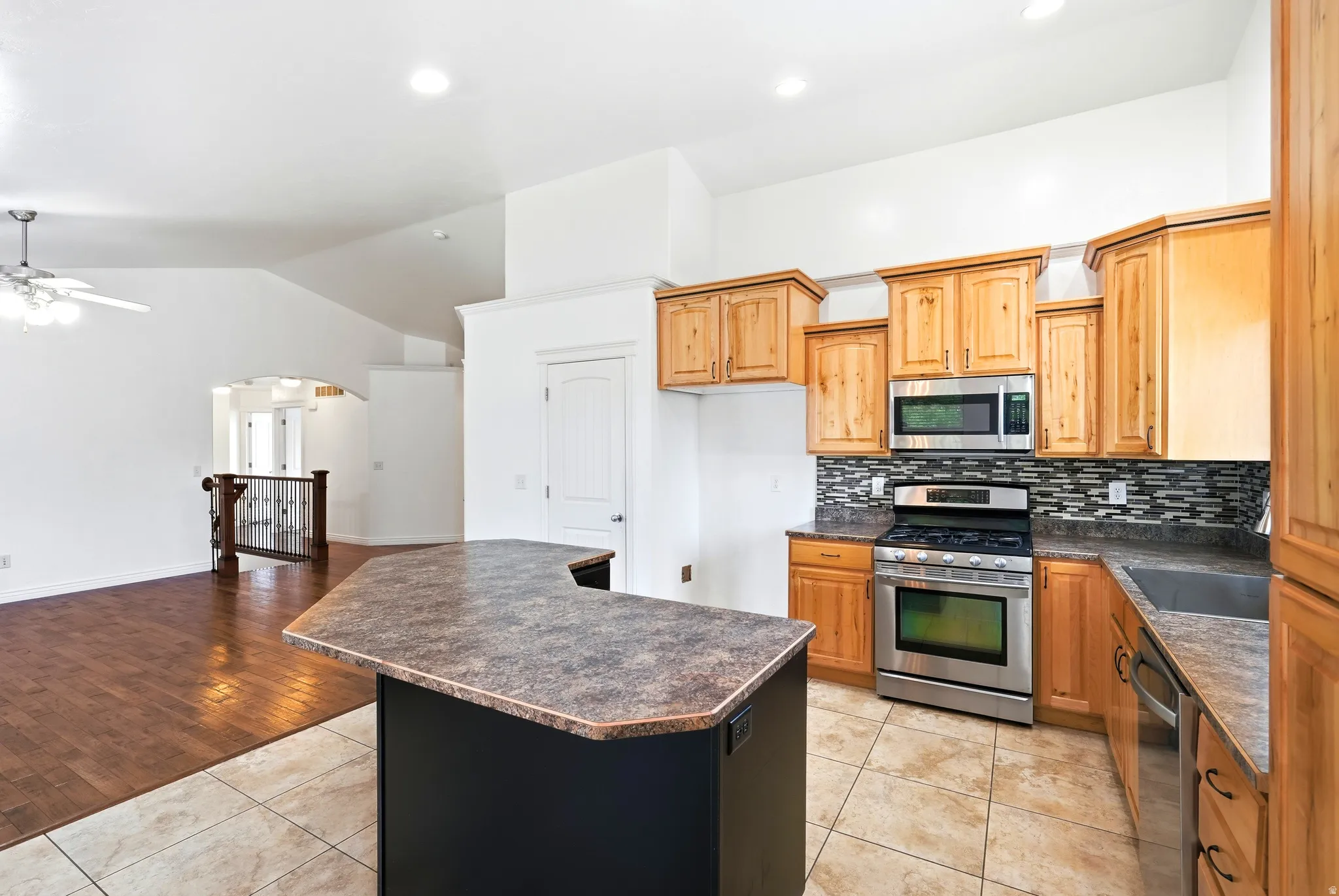 Kitchen featuring a central island with a breakfast bar, light wood cabinetry, stainless steel appliances, and a mosaic tile backsplash