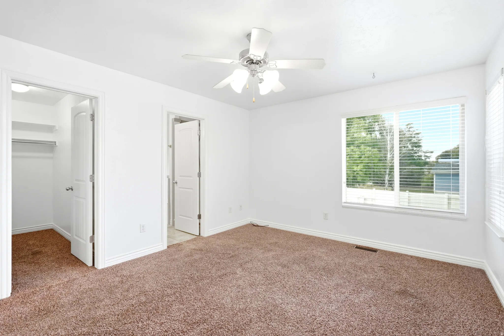Spacious room featuring neutral carpeting, white walls, and a ceiling fan with integrated lighting