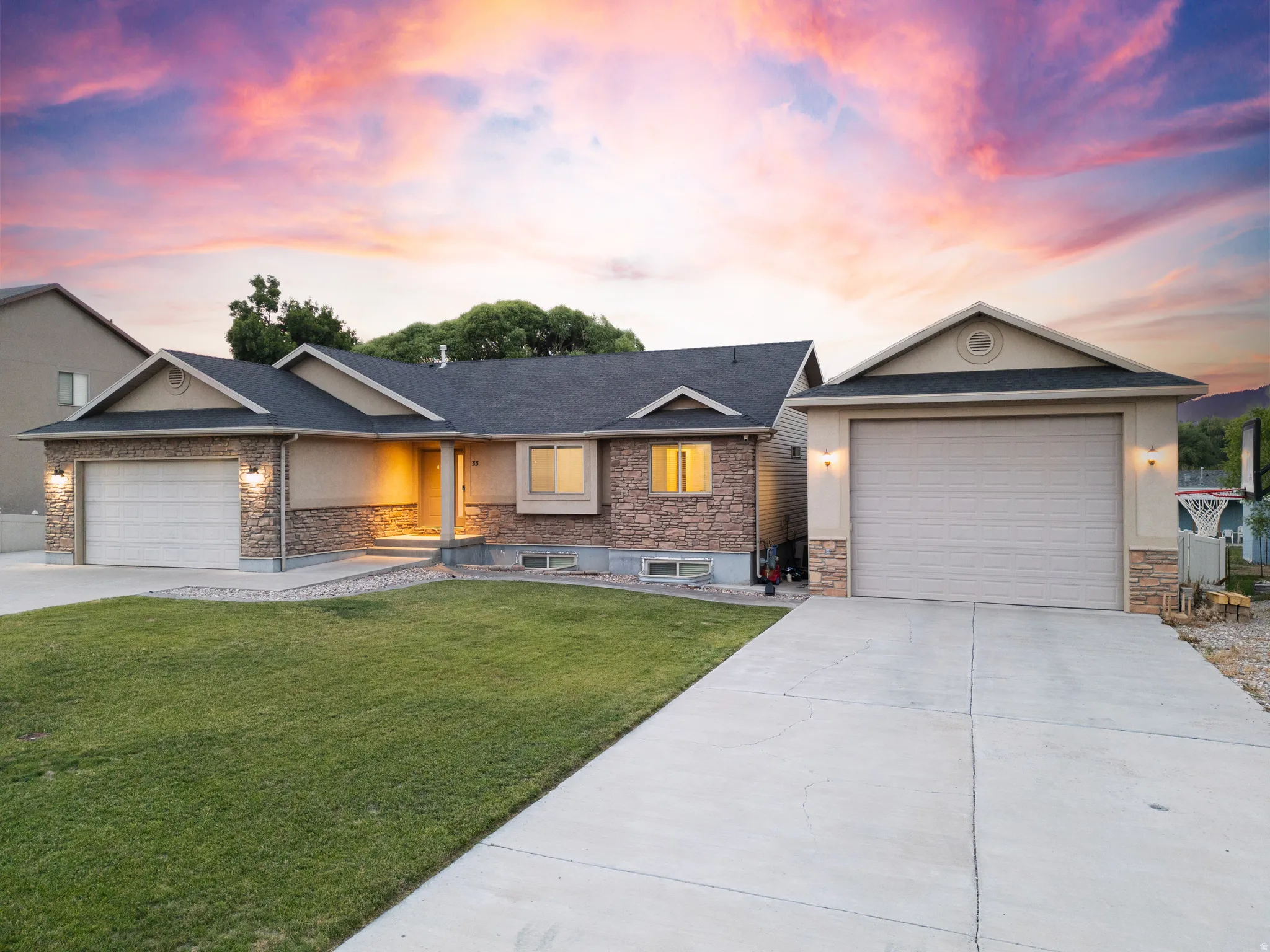 Stucco and stone facade home featuring two separate garage doors, a concrete driveway, and a manicured front lawn