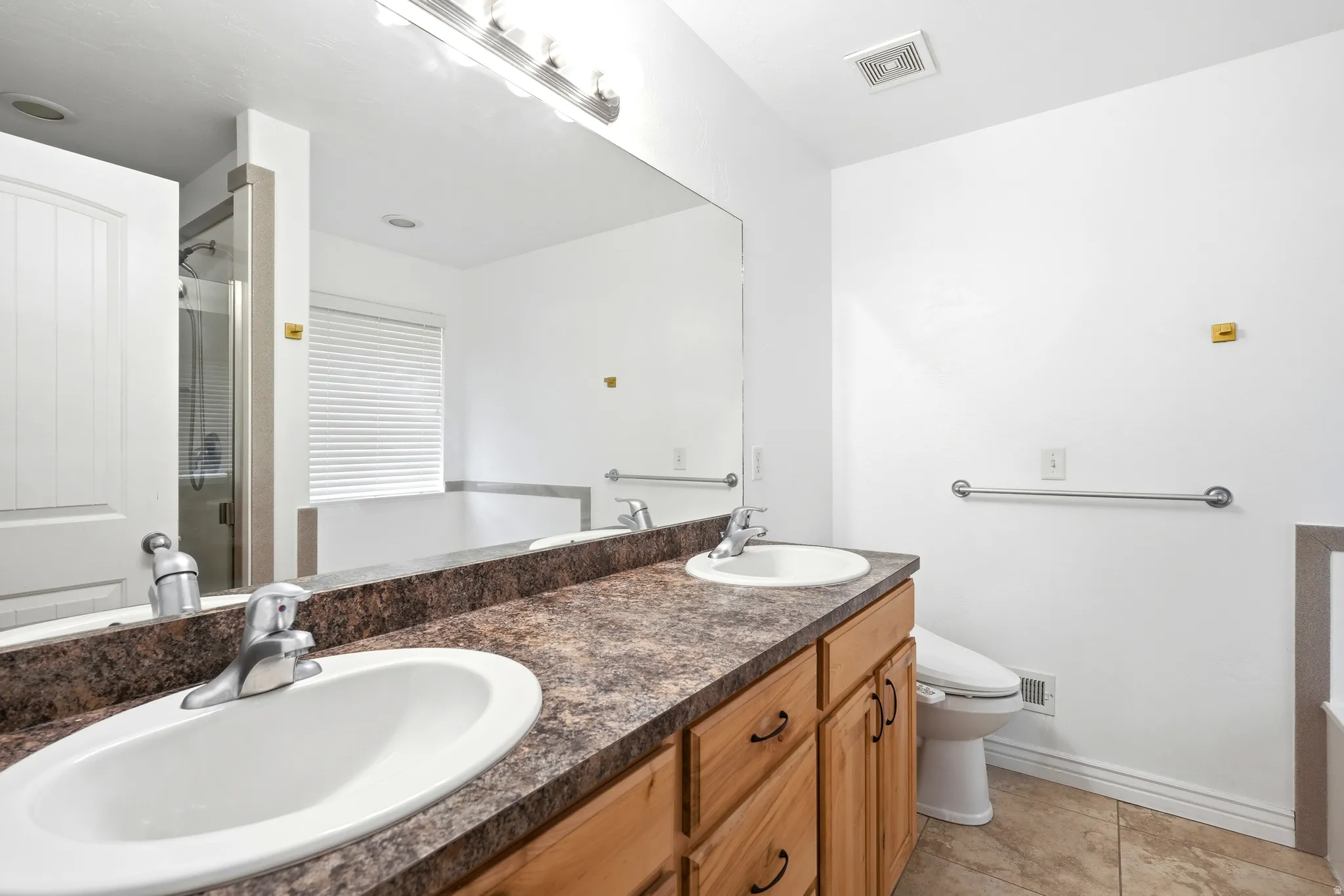 Dual vanity with laminate countertop, natural wood cabinetry, and chrome fixtures