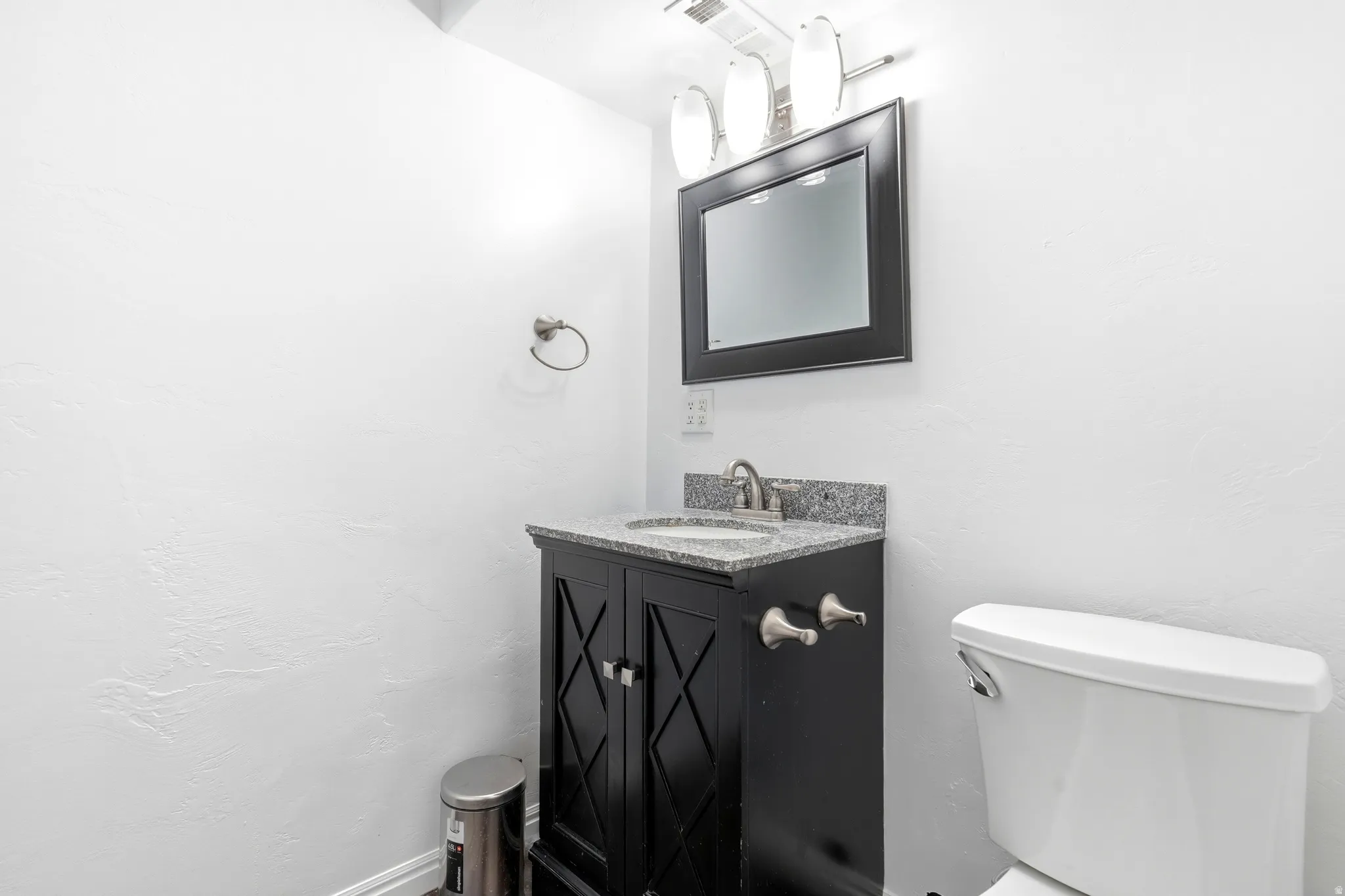 Powder room featuring a black vanity with crosshatch detailing, granite countertop, undermount sink, and framed mirror with a three-bulb vanity light
