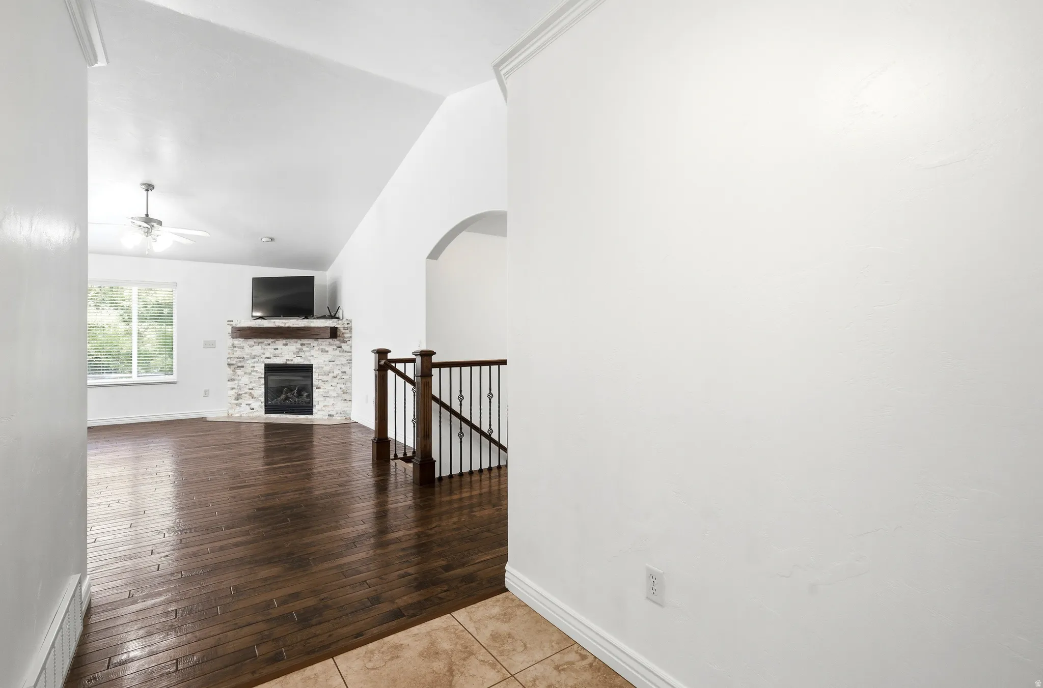 Living area featuring wood-finish flooring, a vaulted ceiling, and a fireplace with a stone surround