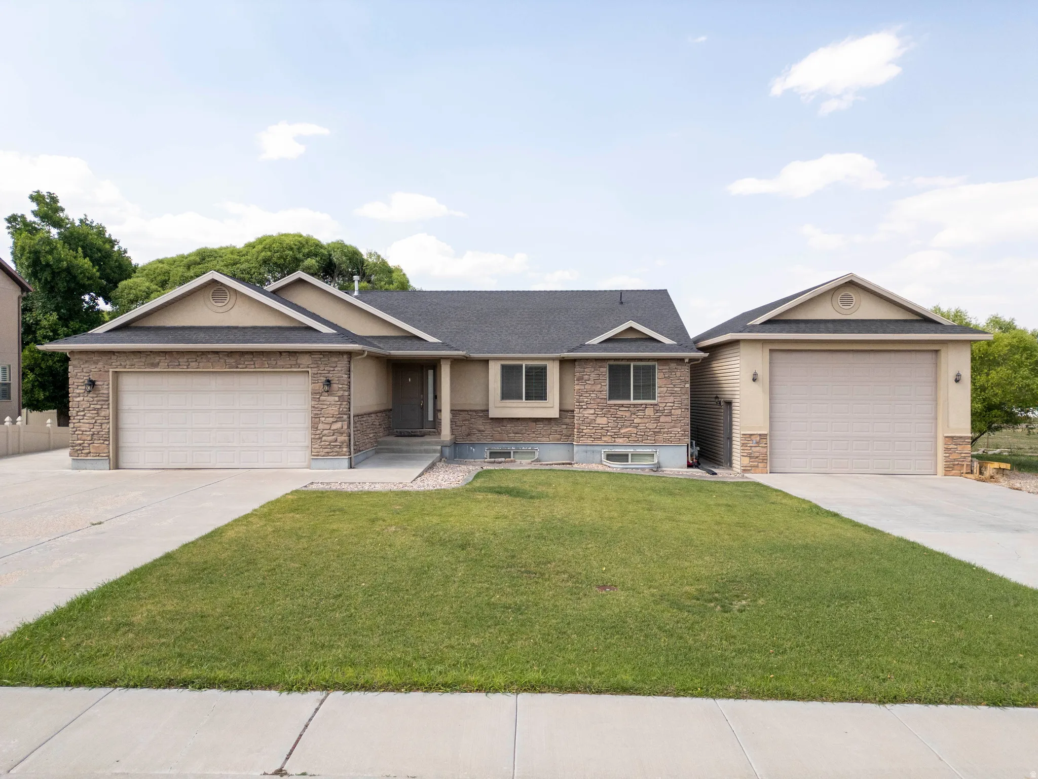 Single-story residence featuring a stone and stucco exterior, dual attached garages with separate driveways, and a dark shingle roof