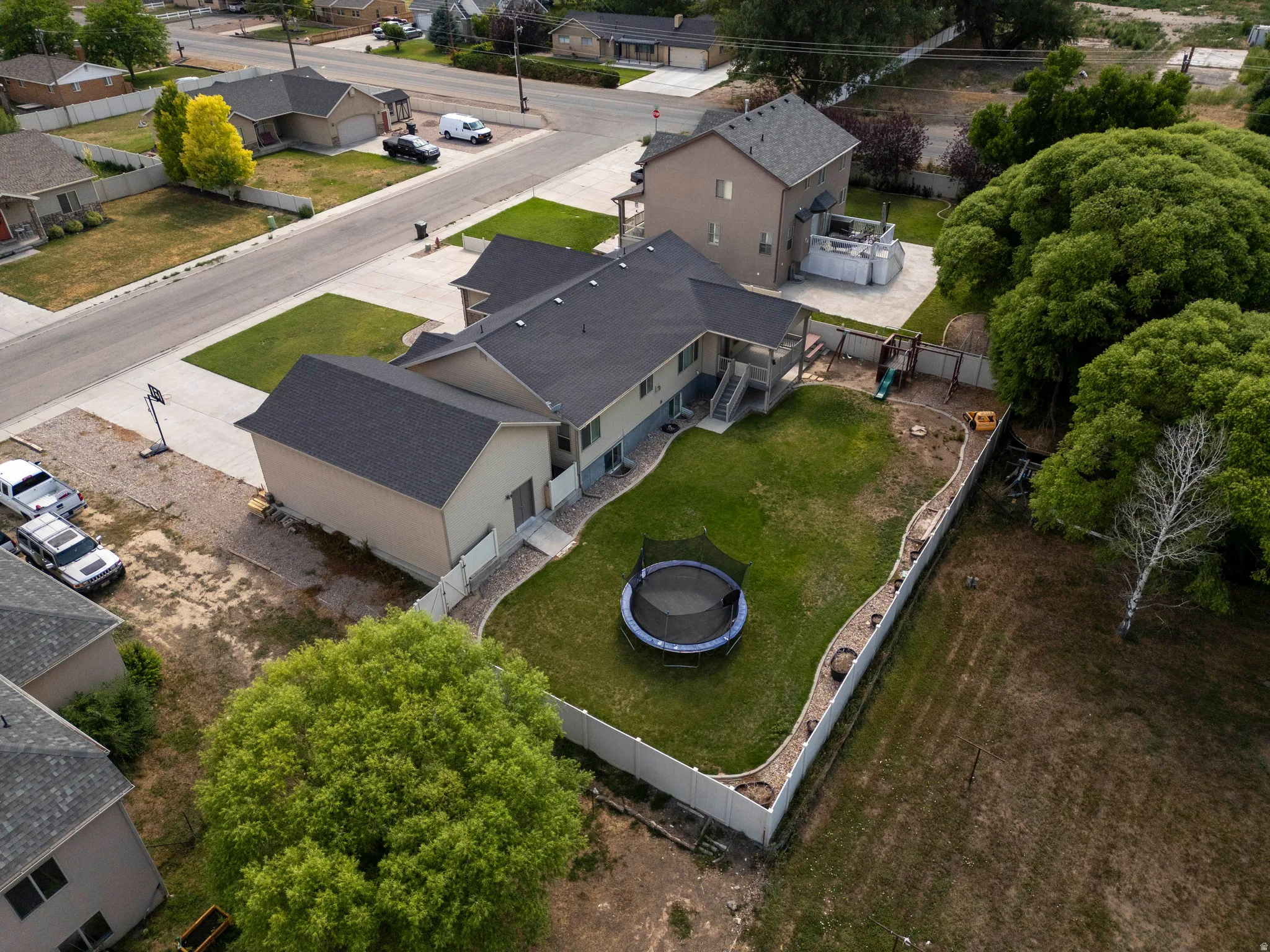 Expansive backyard featuring a manicured lawn, white privacy fence, and mature perimeter trees