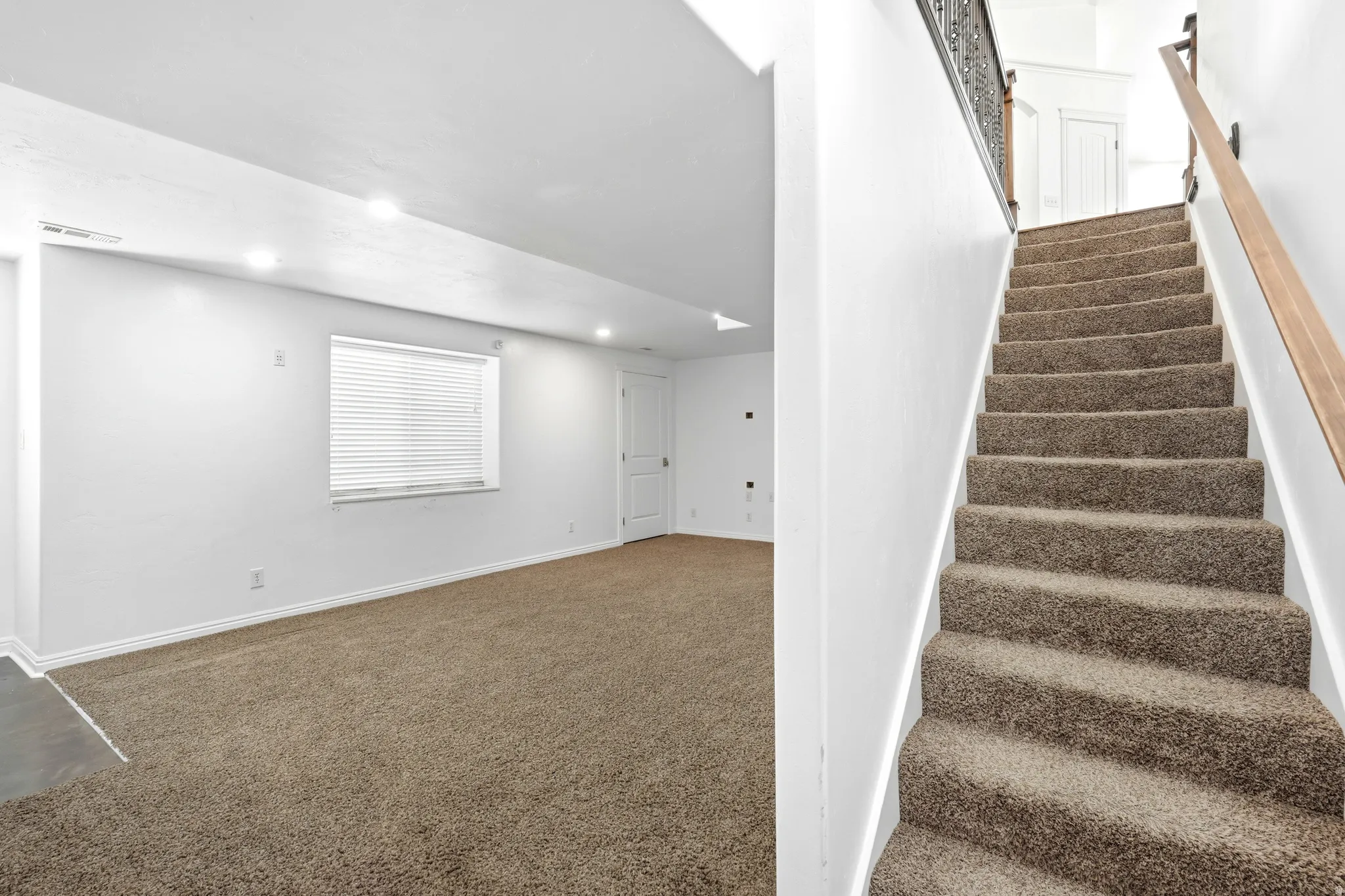 Carpeted staircase with dark metal and wood-finish railing, leading up to a landing with a white door